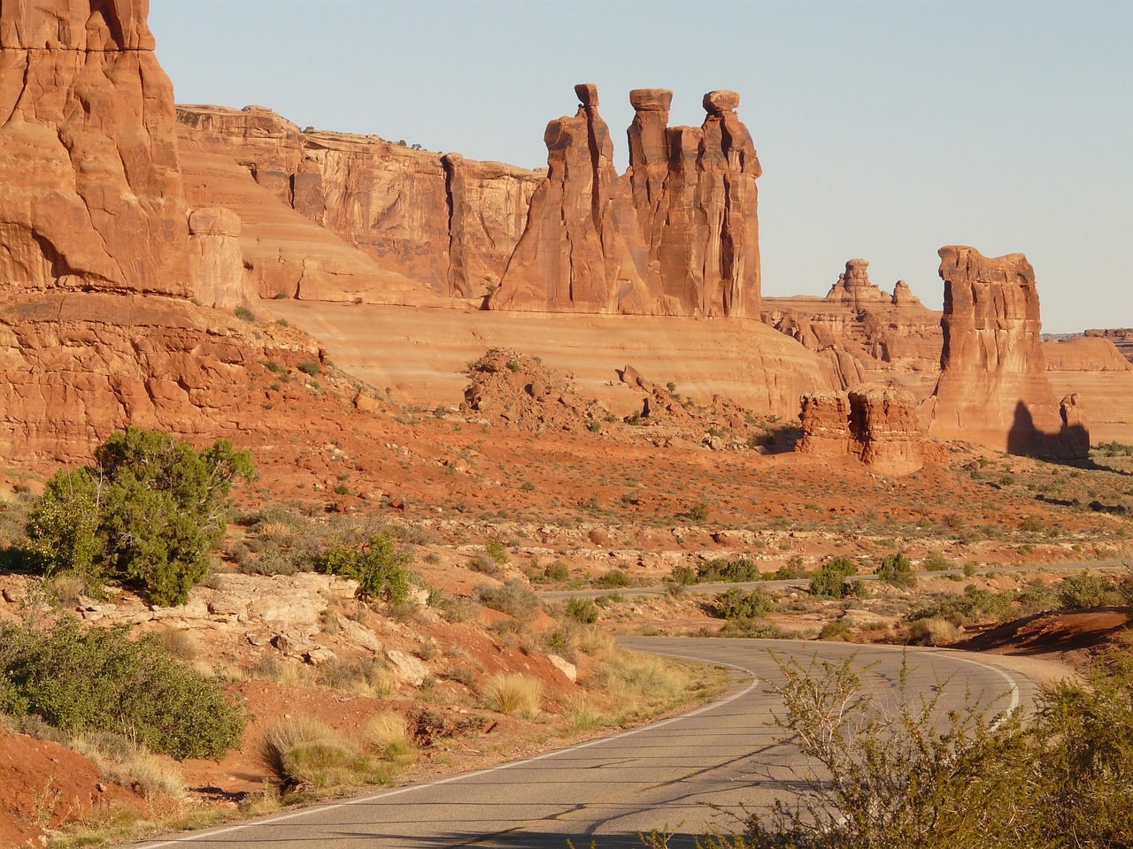 Towers Beside the Scenic Road Tall sandstone towers rising beside a winding paved road through red desert with junipers in the foreground