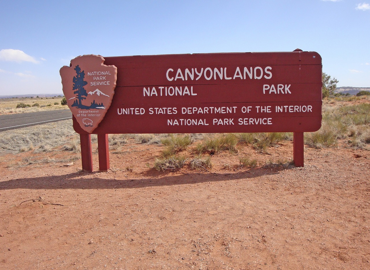 Canyonlands National Park Entrance Sign Red wooden entrance sign reading Canyonlands National Park with the National Park Service arrowhead beside a paved road