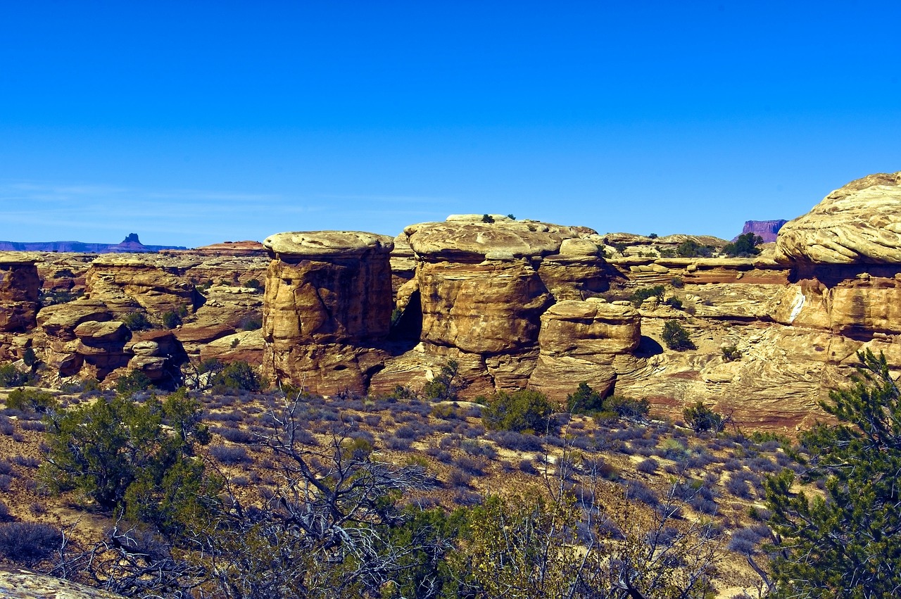 Rounded Sandstone Formations Rounded sandstone formations and a flat mesa edge under a deep blue sky with sparse shrubs
