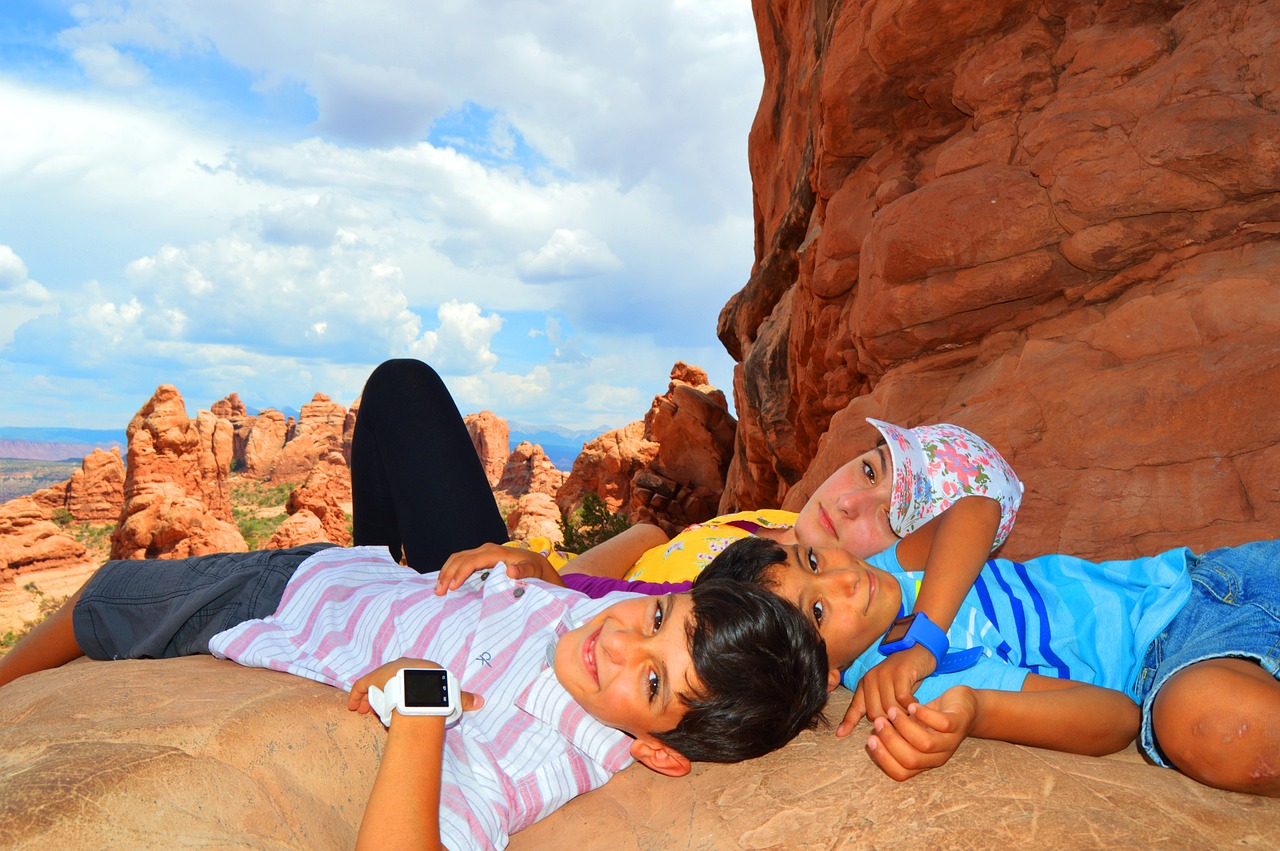 Three children lying side by side on a sandstone ledge above red rock fins