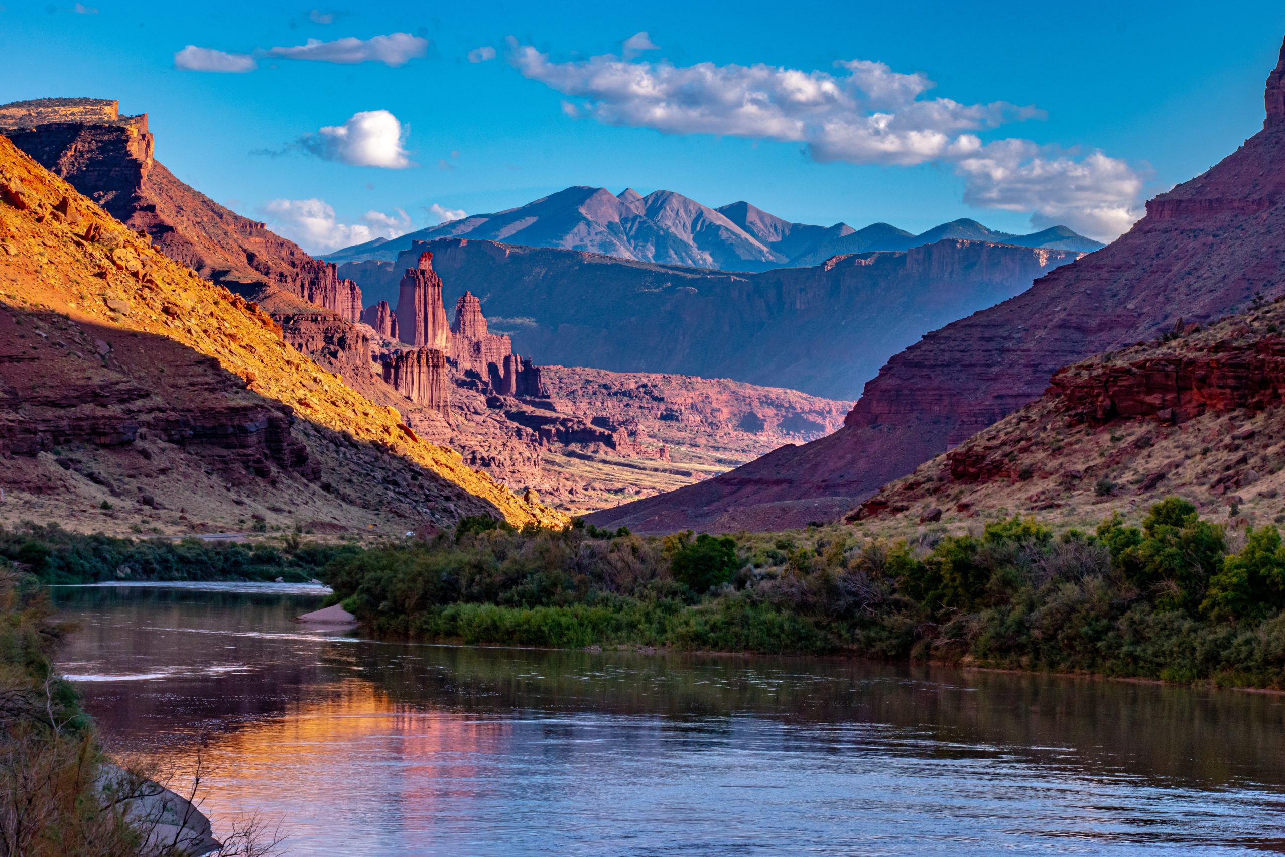 Calm river in a red rock canyon at golden hour, with tall rock spires and mountains in the distance