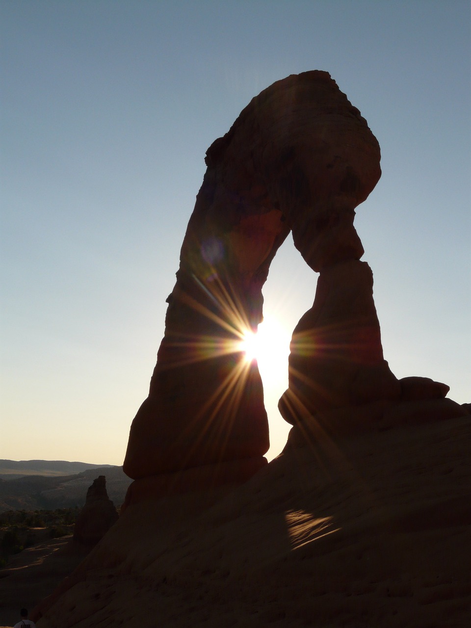 Delicate Arch silhouetted against the sky with the sun flaring through the opening at sunset