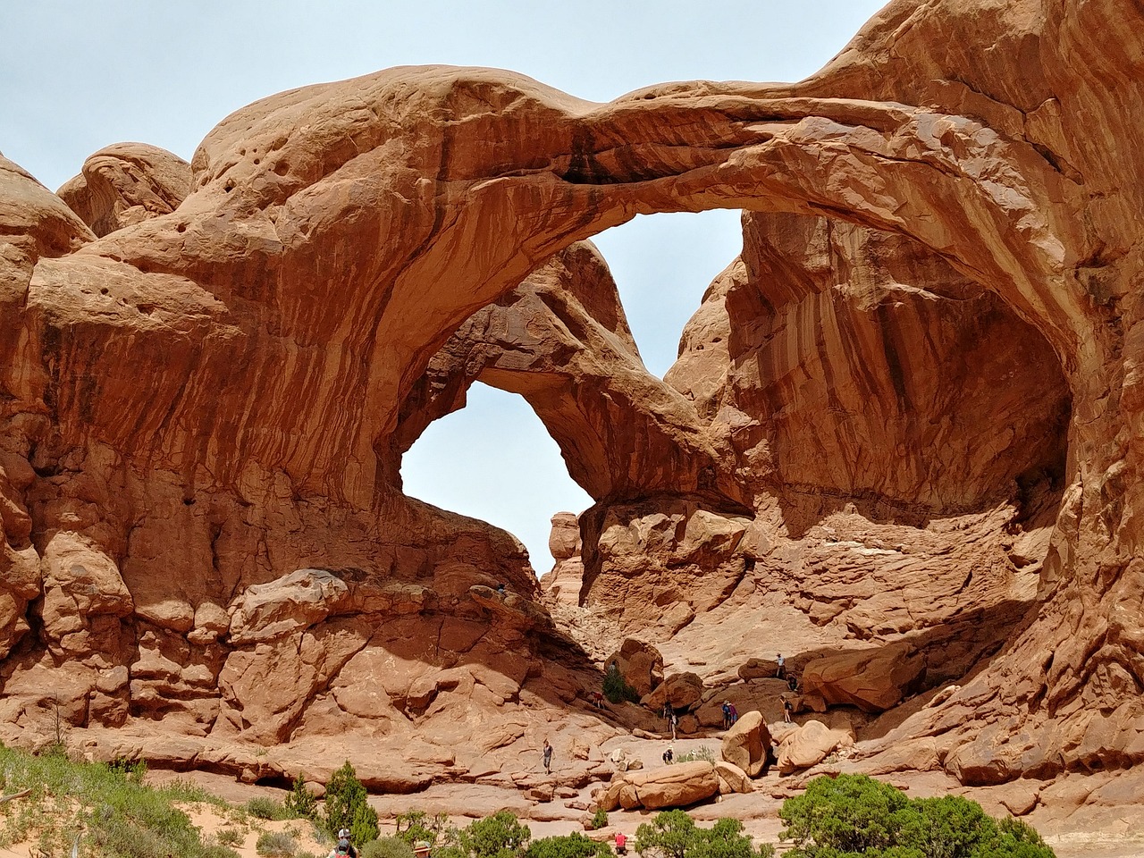 Double Arch with two large openings in red sandstone and small visitors on the boulders at its base