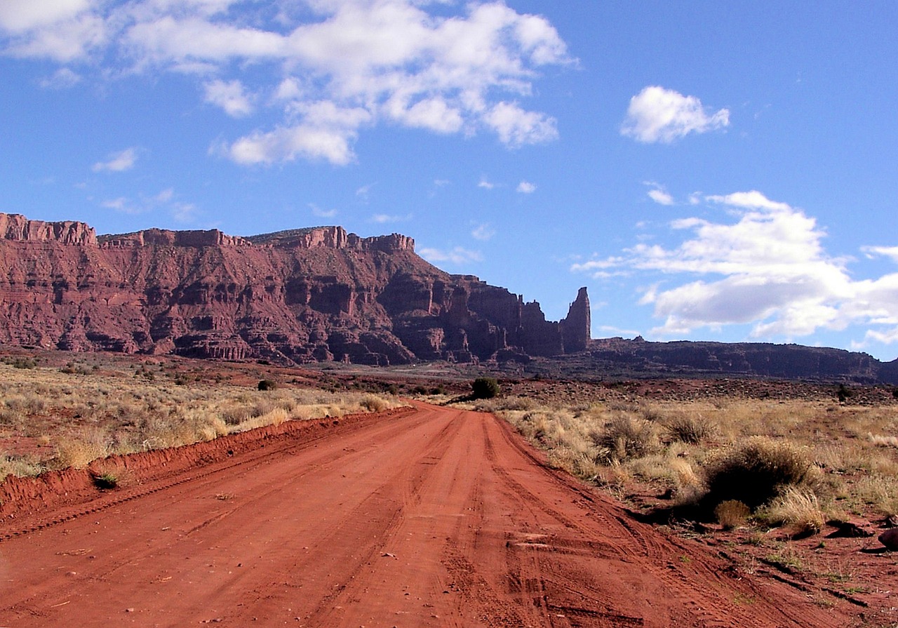Tall banded red rock spires and cliffs of the Fisher Towers rising under a blue sky with clouds