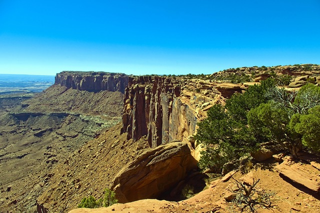 Flat topped mesa and layered red cliffs below a clear blue sky, with a steep drop at the rim