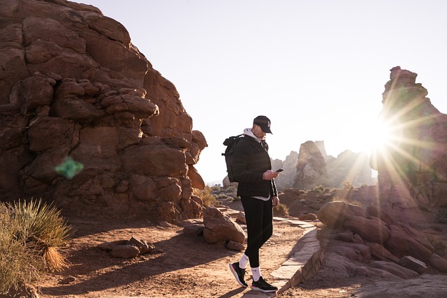 Hiker Checking a Phone at Sunrise Hiker in a dark jacket and cap checking a phone on a sandstone trail with the low sun behind