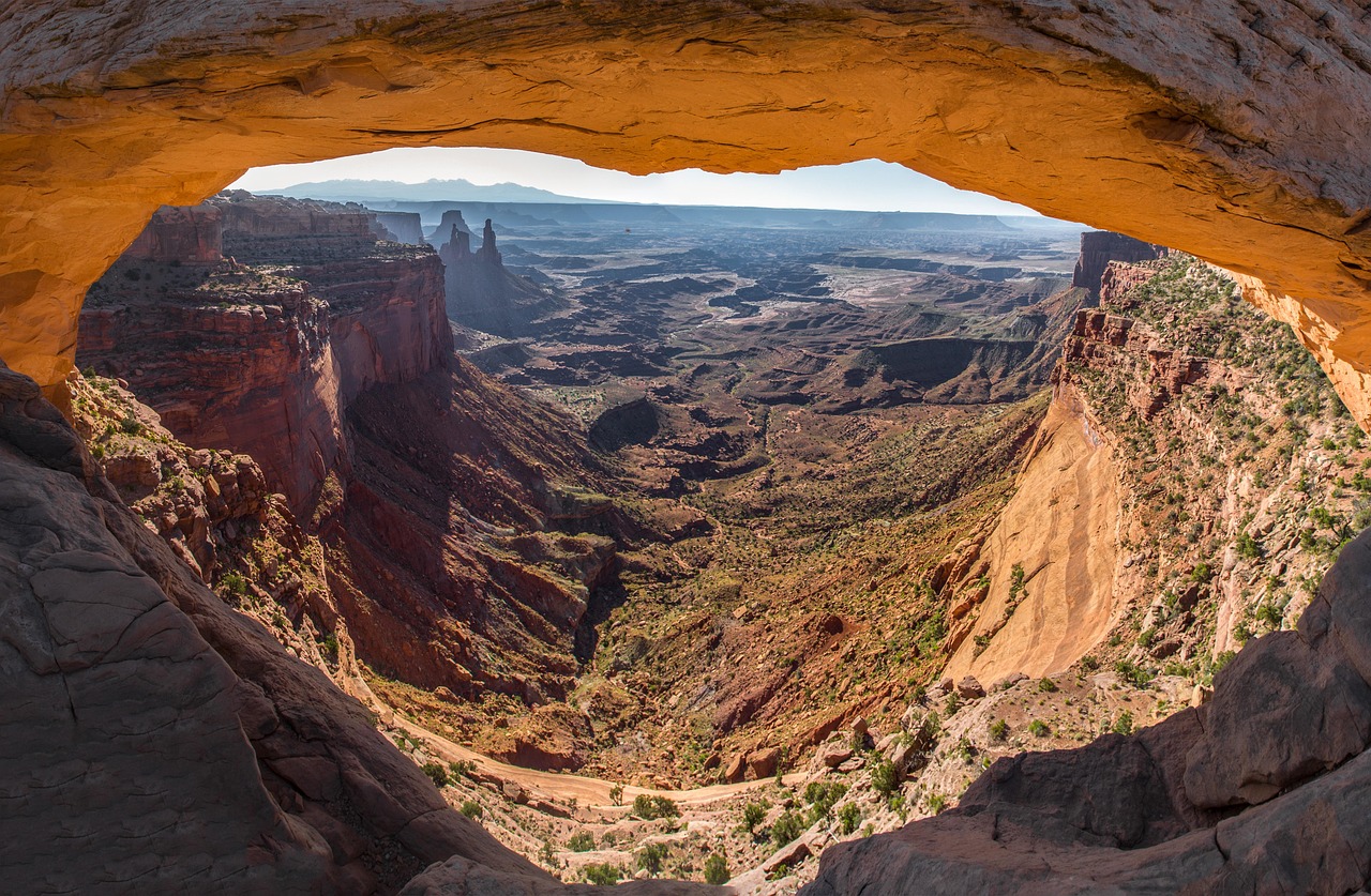 View Through Mesa Arch Orange sandstone underside of Mesa Arch framing a deep canyon with distant spires and a hazy horizon