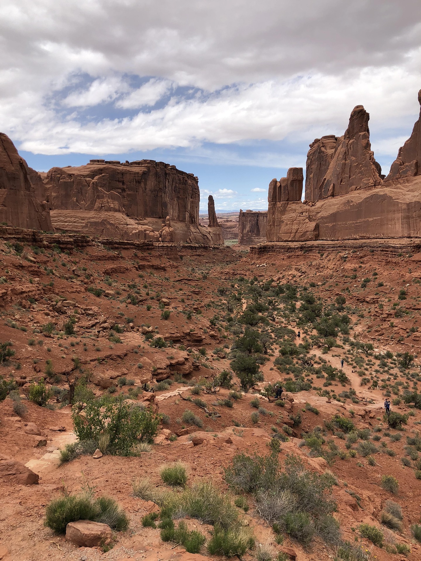 Hikers on a trail below the tall sandstone walls of Park Avenue in Arches National Park